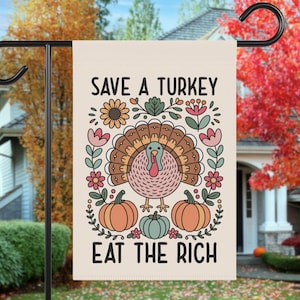 May include: A beige garden flag with a colorful illustration of a turkey, pumpkins, and floral elements. The text "SAVE A TURKEY" and "EAT THE RICH" are displayed in black. The flag is hanging on a black metal stand.