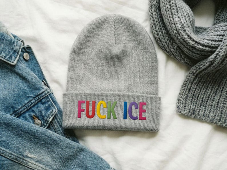 May include: A gray beanie with the embroidered text "FUCK ICE" in rainbow colors. The beanie is folded at the brim and is displayed with a denim jacket and a gray scarf.
