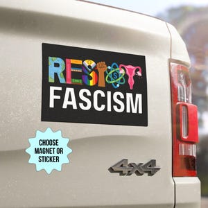 Könnte beinhalten: Ein schwarzer und weißer Automagnet oder Aufkleber mit dem Text "Resist Fascism" in weißen Buchstaben. Das Wort "Resist" besteht aus verschiedenen Symbolen, darunter ein Globus, eine Faust, ein Regenbogen, eine Gebärmutter und ein Atom. Ein kleinerer weißer Aufkleber mit blauem Text lautet "Choose Magnet or Sticker".