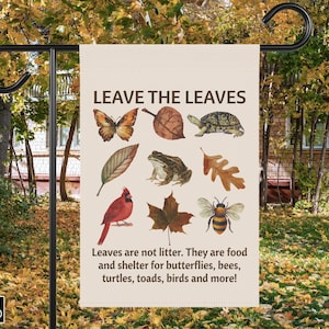 Könnte beinhalten: Eine beige Gartenflagge mit dem Text "LEAVE THE LEAVES" und Illustrationen eines Schmetterlings, Blattes, Schildkröte, Frosches, Kardinals, Biene und mehr. Die Botschaft der Flagge ist, dass Blätter kein Müll sind.
