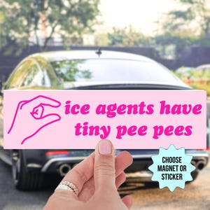 Puede incluir: Un imán o pegatina rectangular rosa con el texto "ice agents have tiny pee pees" en una fuente juguetona. El diseño incluye un gesto con la mano. Un coche está en el fondo.