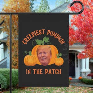 May include: Black Halloween garden flag with the text "Creepiest Pumpkin in the Patch" in orange. The design features a pumpkin with a face and two smaller pumpkins. The flag is displayed outdoors.