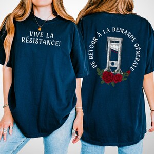 May include: Navy blue t-shirt with white text "VIVE LA RÉSISTANCE!" on the front. The back features a guillotine illustration surrounded by text and red roses. A casual, comfortable tee.