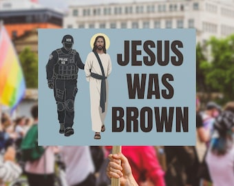 May include: A sign held up in a crowd with the words "JESUS WAS BROWN" in large, dark brown letters. An illustration depicts Jesus being escorted by an ICE officer. A rainbow flag is visible in the background.