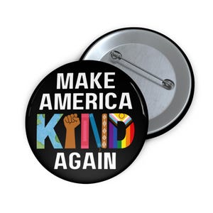 Puede incluir: Un botón negro con el texto "MAKE AMERICA KIND AGAIN" en blanco. La palabra "KIND" está en letras coloridas con un puño, un globo, libros y un arcoíris. Un segundo botón es visible en el fondo.