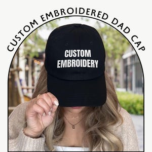 May include: Black dad cap with the words "CUSTOM EMBROIDERY" in white block letters. The cap is part of a custom embroidered dad cap collection. The words "CUSTOM EMBROIDERED DAD CAP" are arched above the cap.