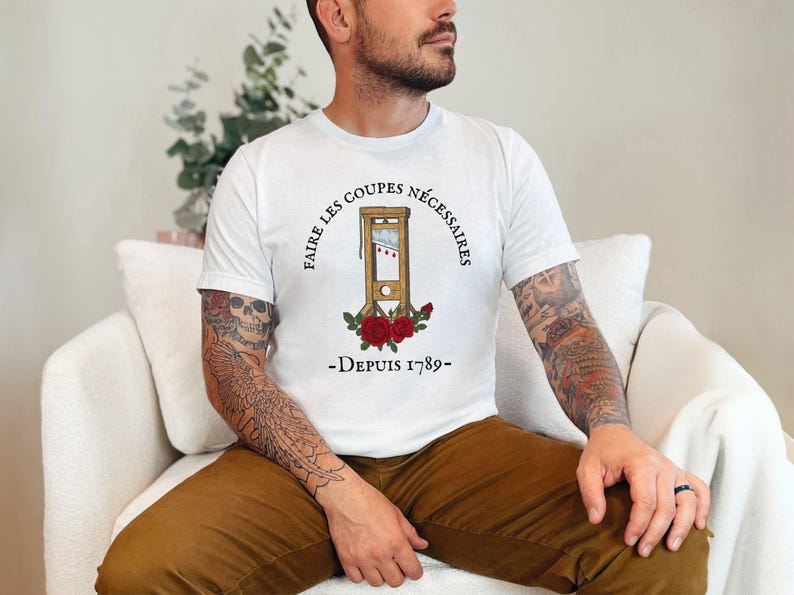 Puede incluir: Camiseta blanca con una ilustraci&oacute;n en blanco y negro de una guillotina con rosas rojas y el texto "Faire les coupes necessaires - Depuis 1789 - "