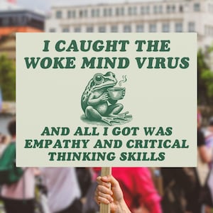 May include: A sign held up in a crowd with the text "I CAUGHT THE WOKE MIND VIRUS AND ALL I GOT WAS EMPATHY AND CRITICAL THINKING SKILLS." The sign has a green frog illustration holding a cup.