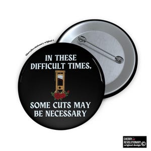 May include: A black button with white text reading "IN THESE DIFFICULT TIMES, SOME CUTS MAY BE NECESSARY". The design includes a guillotine illustration and red roses. The button is round with a pin on the back.