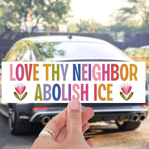 May include: A rectangular sticker with the text "LOVE THY NEIGHBOR ABOLISH ICE" in colorful block letters. The sticker is held in front of a car. Floral illustrations are on the sticker.