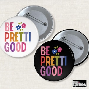 Pode incluir: Dois botões redondos, um branco e outro preto, com a frase "BE PRETTI GOOD" em cores do arco-íris. O botão branco tem detalhes florais azuis e rosa. O botão preto tem motivos florais semelhantes.