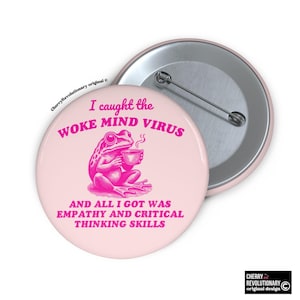 Può includere: Un bottone rosa chiaro con un'illustrazione di una rana rosa che tiene una tazza. Il testo sul bottone recita: "Ho preso il WOKE MIND VIRUS E TUTTO QUELLO CHE HO OTTENUTO È STATA EMPATIA E CAPACITÀ DI PENSIERO CRITICO."
