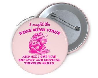 May include: A light pink button with a pink frog illustration holding a cup of coffee. The text on the button reads "I caught the WOKE MIND VIRUS AND ALL I GOT WAS EMPATHY AND CRITICAL THINKING SKILLS."