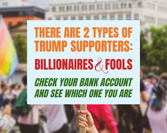 May include: A sign held up in a crowd with the text "THERE ARE 2 TYPES OF TRUMP SUPPORTERS: BILLIONAIRES & FOOLS CHECK YOUR BANK ACCOUNT AND SEE WHICH ONE YOU ARE" in orange, red, and green.