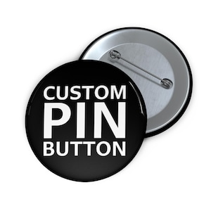 May include: A black button with white text that reads "CUSTOM PIN BUTTON". The back of the button is silver with a safety pin.