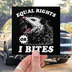 May include: Black and white sticker with a cartoon opossum with its mouth open and the text "Equal Rights or I Bites".