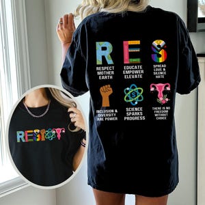 May include: Black t-shirt with the word "RESIST" in colorful letters. The back of the shirt features the word "RES" with various graphics and phrases: "Respect Mother Earth," "Educate Empower Elevate," and "Spread Love & Silence Hate."