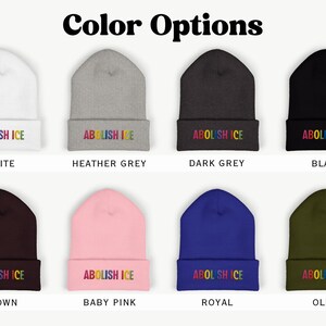May include: A selection of eight beanies in various colors, including white, heather grey, dark grey, black, brown, baby pink, royal blue, and olive green. Each beanie displays the text "ABOLISH ICE" in rainbow-colored embroidery.