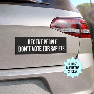以下が含まれることがあります： 「Decent People Don't Vote For Rapists」と書かれた白黒のバンパーステッカー。ステッカーは銀色の車に貼られています。青い星形のステッカーに「Choose Magnet or Sticker」という文字が書かれています。