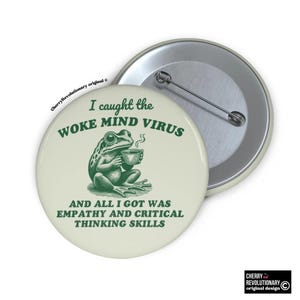 Peut inclure: Une grenouille verte portant une chemise verte et tenant une tasse de café. Le texte sur le bouton dit "J'ai attrapé le virus de l'esprit éveillé et tout ce que j'ai eu, c'est de l'empathie et des compétences de pensée critique".