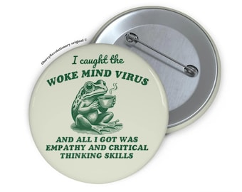 May include: A green frog wearing a green shirt and holding a cup of coffee. The text on the button reads "I caught the woke mind virus and all I got was empathy and critical thinking skills".