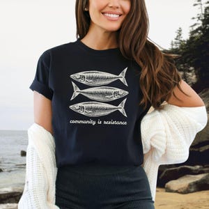 May include: Black t-shirt with a graphic of three fish and the text "community is resistance".