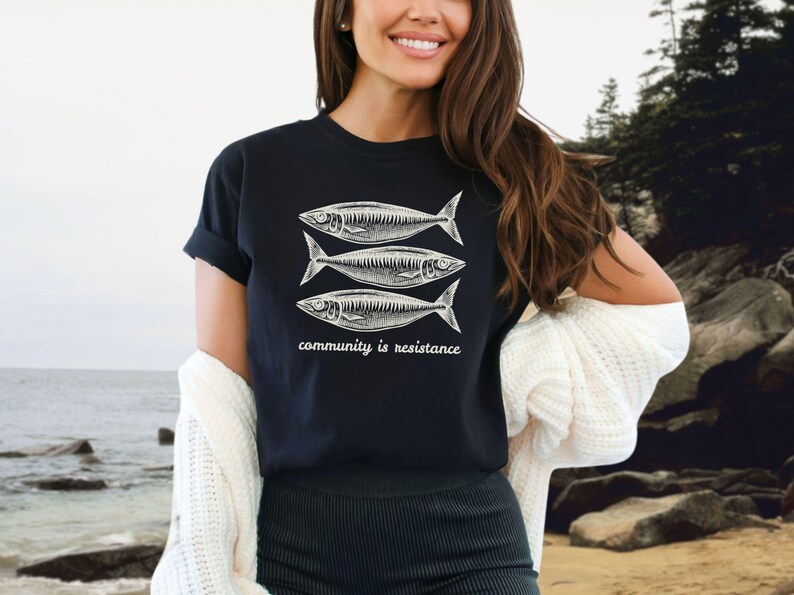 May include: Black t-shirt with a graphic of three fish and the text "community is resistance".