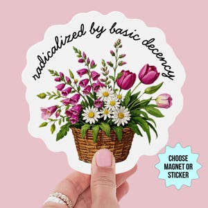 Könnte beinhalten: Ein weißer Aufkleber mit gewelltem Rand mit einer Illustration eines Blumenkorbs. Der Korb enthält rosa Fingerhutblumen, weiße Gänseblümchen und lila Tulpen. Der Text "radicalized by basic decency" ist über den Blumen angeordnet.