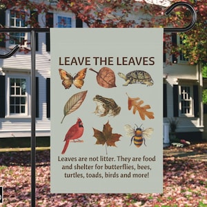 Puede incluir: Una bandera de jardín con el texto "LEAVE THE LEAVES" e ilustraciones de una mariposa, hoja, tortuga, rana, cardenal, abeja y más. El mensaje de la bandera es que las hojas son alimento y refugio para la vida silvestre.