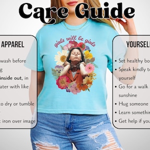 May include: Light blue t-shirt with the text "girls will be girls" and a floral graphic. The shirt features a care guide with washing instructions and self-care tips. The image includes text about apparel and self-care.