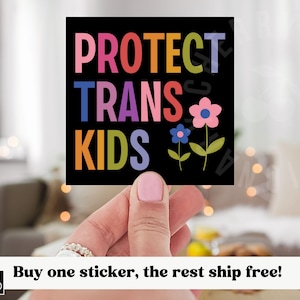 以下が含まれることがあります： カラフルな文字で「PROTECT TRANS KIDS」と書かれた黒い正方形のステッカー。緑の茎と葉を持つ2つの花も描かれています。ステッカーは人が持っています。