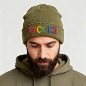 May include: Olive green beanie with the embroidered text "FUCK ICE" in rainbow colors. The beanie is made of a soft, knitted material. The person wearing the beanie is also wearing an olive green hoodie.