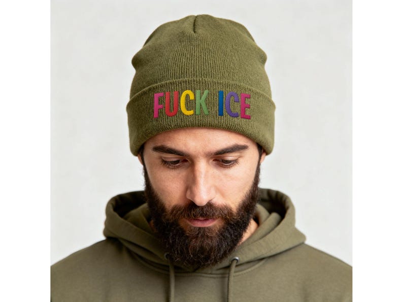 May include: Olive green beanie with the embroidered text "FUCK ICE" in rainbow colors. The beanie is made of a soft, knitted material. The person wearing the beanie is also wearing an olive green hoodie.