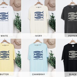 May include: A set of ten t-shirts in various colors, each featuring a graphic of three fish with the text "community is resilience". The colors include white, ivory, pepper, butter, and Chambray.