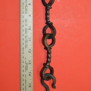 Peut inclure: Une chaîne en métal noir avec cinq maillons torsadés, chacun avec une boucle décorative. La chaîne est mesurée à l'aide d'une règle, montrant qu'elle mesure environ 45,7 cm de long.