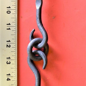 May include: A pair of black metal hooks with a decorative twist design. The hooks are approximately 12 inches long and are shown against a red background.