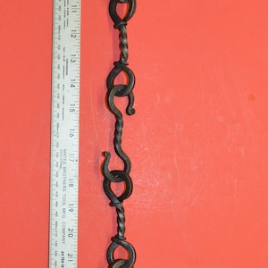 Peut inclure: Une longue chaîne en métal torsadée avec plusieurs boucles et crochets. La chaîne mesure environ 81 cm de long et est présentée sur un fond rouge.