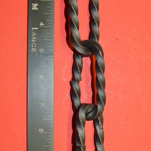 May include: A close-up of a black metal chain with a twisted design. The chain is about 12 inches long and is measured against a ruler.