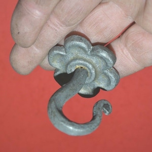 May include: A silver metal hook with a decorative flower-shaped top. The hook is designed for hanging items.