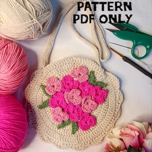 May include: A crocheted bag with a floral design in pink and green. The bag has a long strap and is made with beige yarn. The text "PATTERN PDF ONLY" is visible in the image.