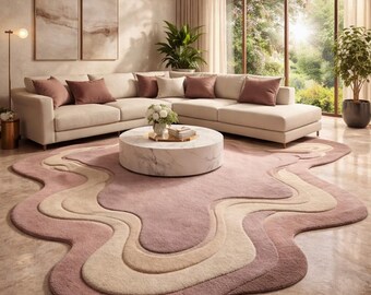 Op de afbeelding: Een woonkamer met een crèmekleurige hoekbank en bordeauxrode kussens. Een ronde marmeren salontafel staat op een uniek tapijt in roze en beige tinten. Het tapijt heeft een abstract, vloeiend ontwerp. De kamer heeft grote ramen.