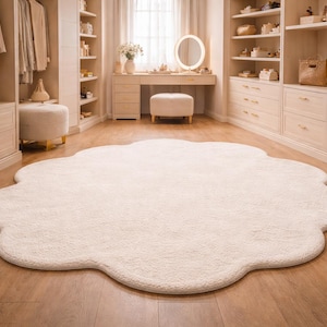 Könnte beinhalten: Ein großer, cremefarbener, wolkenförmiger Teppich liegt auf einem Hartholzboden in einem gut beleuchteten Raum. Die weiche Textur des Teppichs kontrastiert mit dem glatten Boden. Der Raum verfügt über Einbauschränke, einen Schminktisch und ein Fenster.