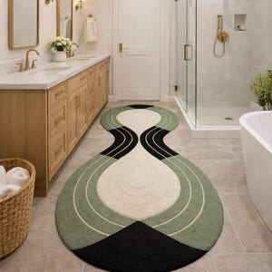 May include: A decorative bathroom rug with an abstract design. The rug has a central off-white shape, bordered by black and green. The rug measures approximately 152 cm long and 76 cm wide.