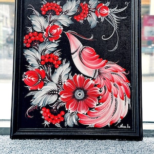 Puede incluir: Pintura enmarcada que presenta un ave estilizada con plumaje rojo y rosa, rodeada de bayas rojas y flores con hojas grises y blancas, sobre un fondo negro. La obra de arte est&aacute; en un marco negro.