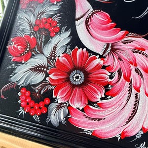 Puede incluir: Pintura enmarcada con un dise&ntilde;o de p&aacute;jaro y flores. La obra presenta un fondo negro con un p&aacute;jaro estilizado en tonos rosas y rojos, rodeado de flores rojas, bayas y hojas grises. El marco es negro.