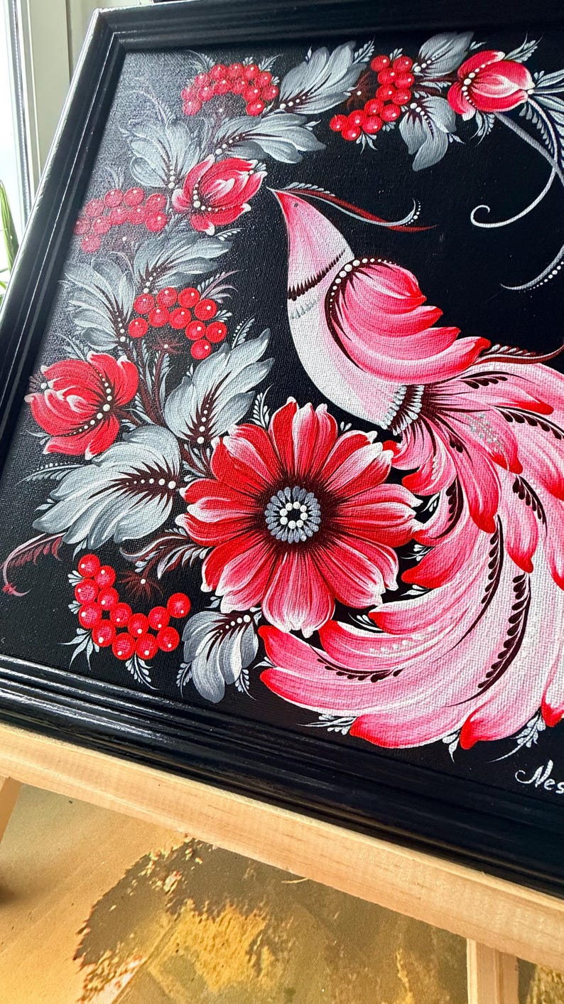 Puede incluir: Pintura enmarcada con un dise&ntilde;o de p&aacute;jaro y flores. La obra presenta un fondo negro con un p&aacute;jaro estilizado en tonos rosas y rojos, rodeado de flores rojas, bayas y hojas grises. El marco es negro.