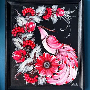 Puede incluir: Pintura enmarcada que presenta un p&aacute;jaro rosa con una larga cola, rodeado de flores rojas, bayas y hojas grises y blancas, sobre un fondo negro. La obra de arte est&aacute; en un marco negro.