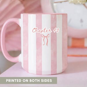 May include: A white ceramic mug with pink stripes and a pink handle. The mug features the text "Chapter 40" with a bow graphic. The words "PRINTED ON BOTH SIDES" are at the bottom of the image. The mug is on a pink surface.