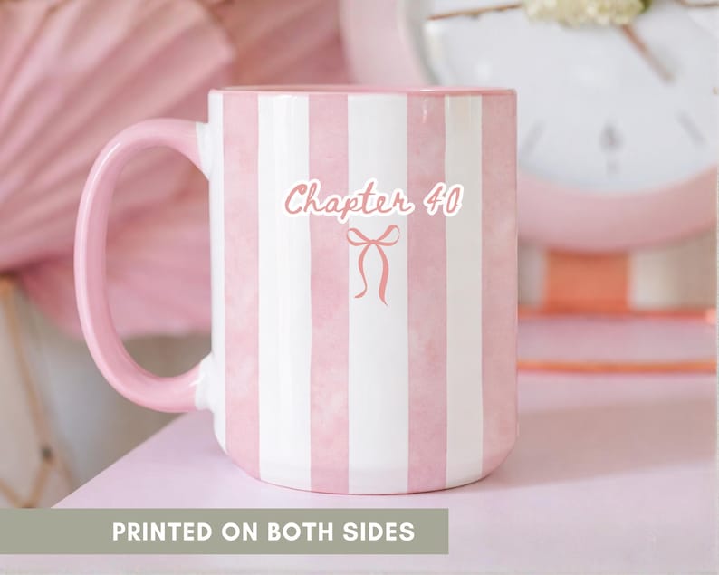 May include: A white ceramic mug with pink stripes and a pink handle. The mug features the text "Chapter 40" with a bow graphic. The words "PRINTED ON BOTH SIDES" are at the bottom of the image. The mug is on a pink surface.