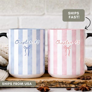 May include: Two ceramic mugs with black handles. One mug is blue and white striped, the other is pink and white striped. Both mugs have the text "Chapter 40" and a bow graphic. The mugs are on a wooden surface.